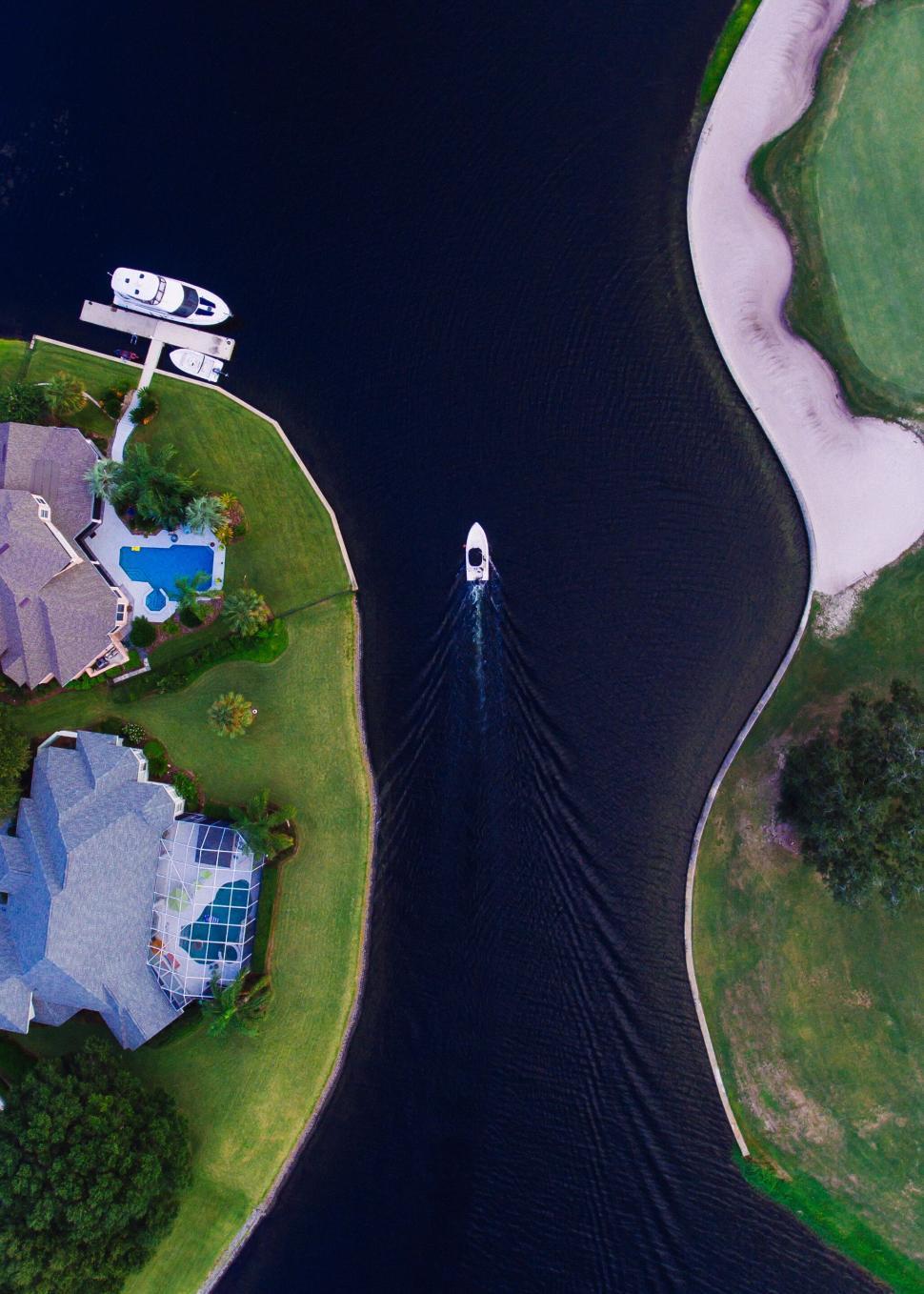 Free Image of Aerial boat on narrow waterway flanked by houses and green lawns 