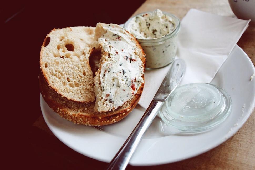 Free Image of Freshly baked bagel with herb cream cheese on a white plate. 