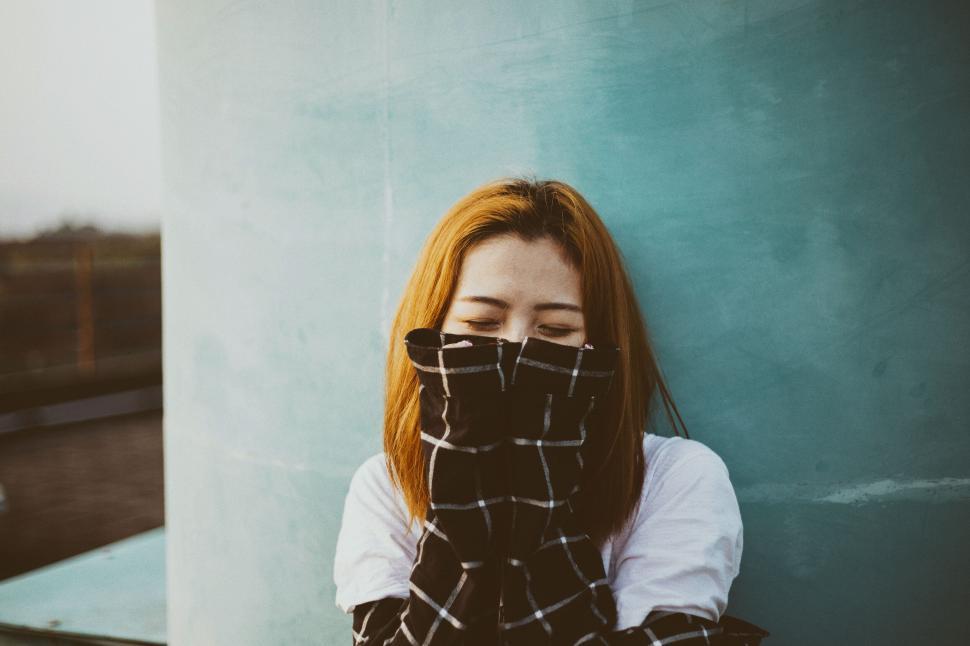 Free Image of Person with glasses leaning against a blue wall, face covered 