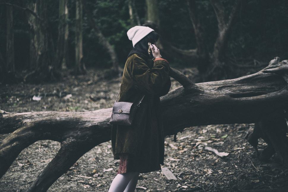 Free Image of Person in Winter Clothes Talking on Phone Beside Fallen Tree 