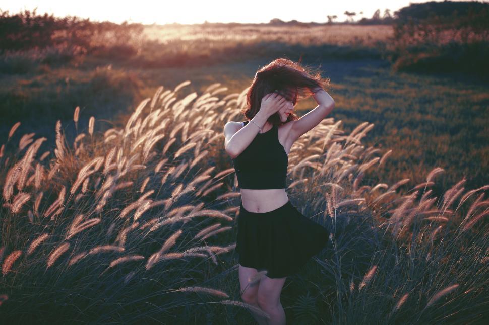 Free Image of Woman standing in field of grass at sunset wearing black outfit. 