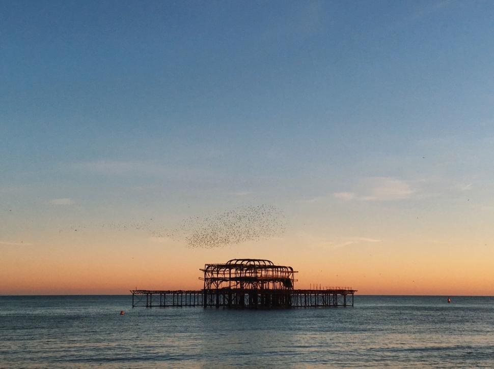 Free Image of Silhouette of an old pier during sunset over a calm ocean horizon. 