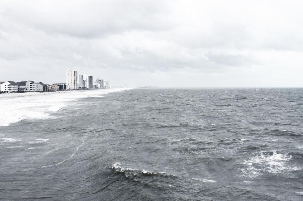 Free Image of Expansive ocean view with a distant city skyline on a cloudy day. 