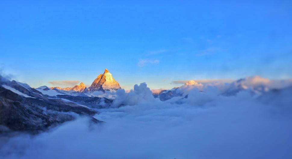 Free Image of Majestic mountain peak rising above clouds in a vivid sunrise sky. 