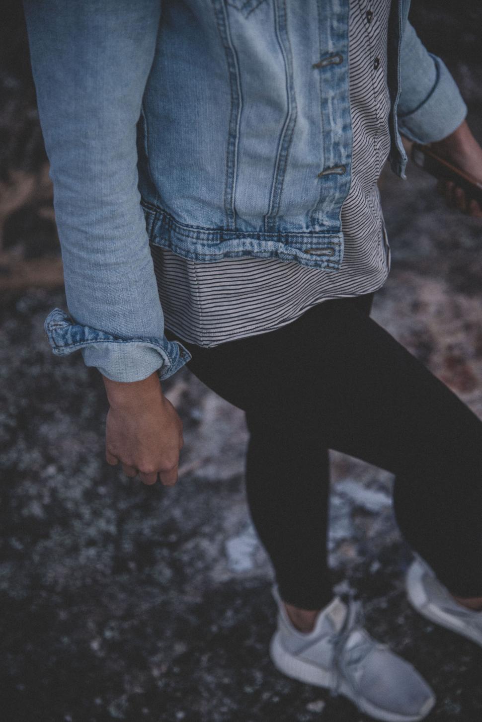 Free Image of Person wearing denim jacket and sneakers walking on rocky path. 