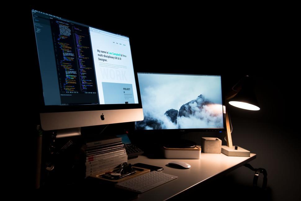 Free Image of Dual monitor computer setup in a dimly lit modern workspace. 