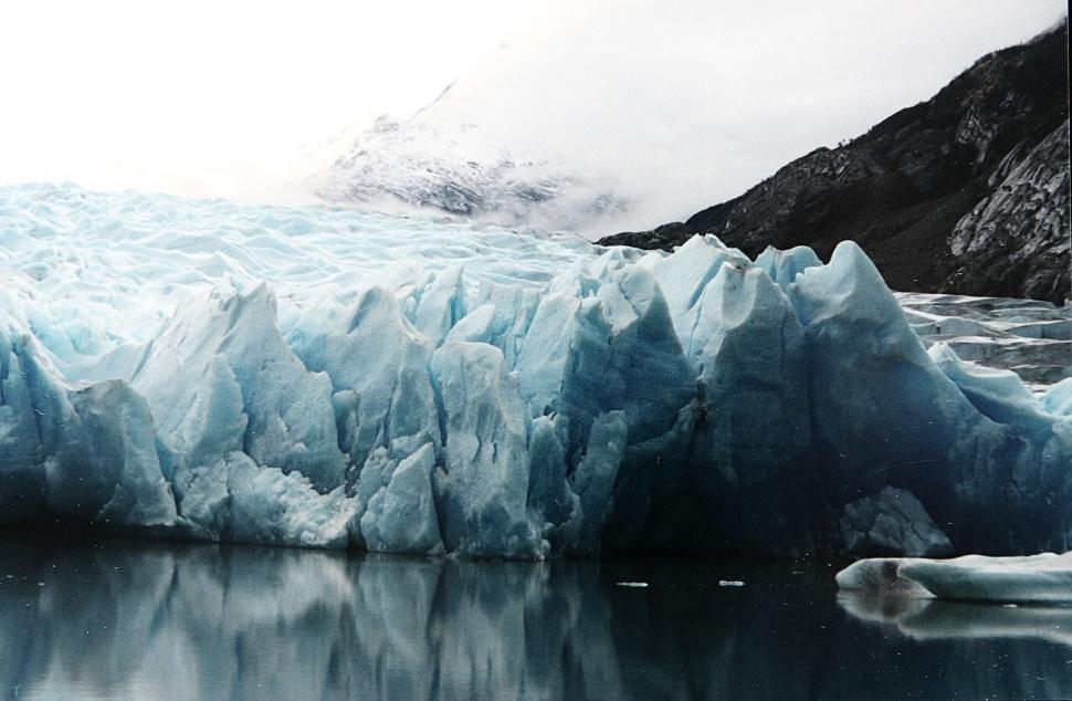Free Image of Glacier ice reflecting in calm water with snowy mountain backdrop. 