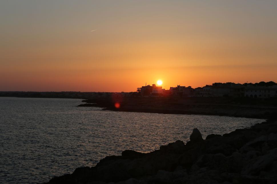 Free Image of Sunset over the coastline with dark silhouettes of buildings and rocks. 