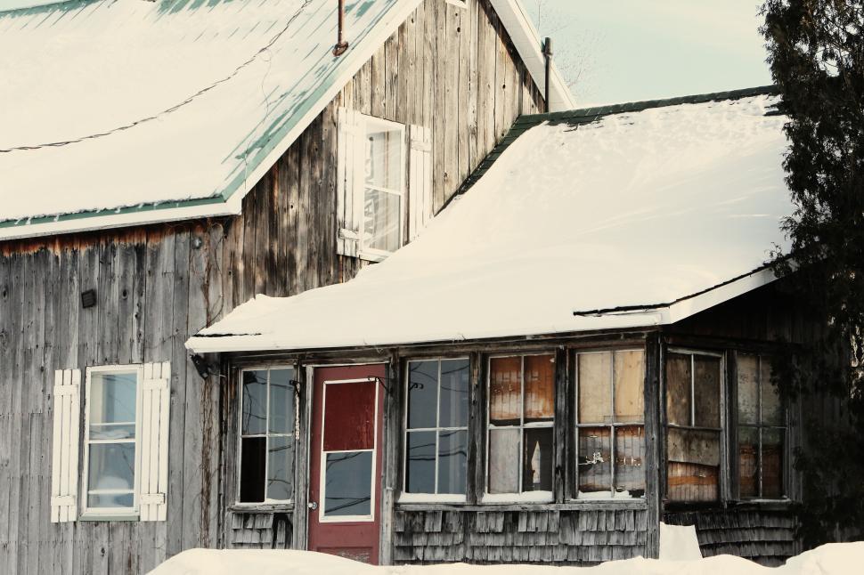 Free Image of Rustic winter cabin with snow-covered roof and weathered wood facade 