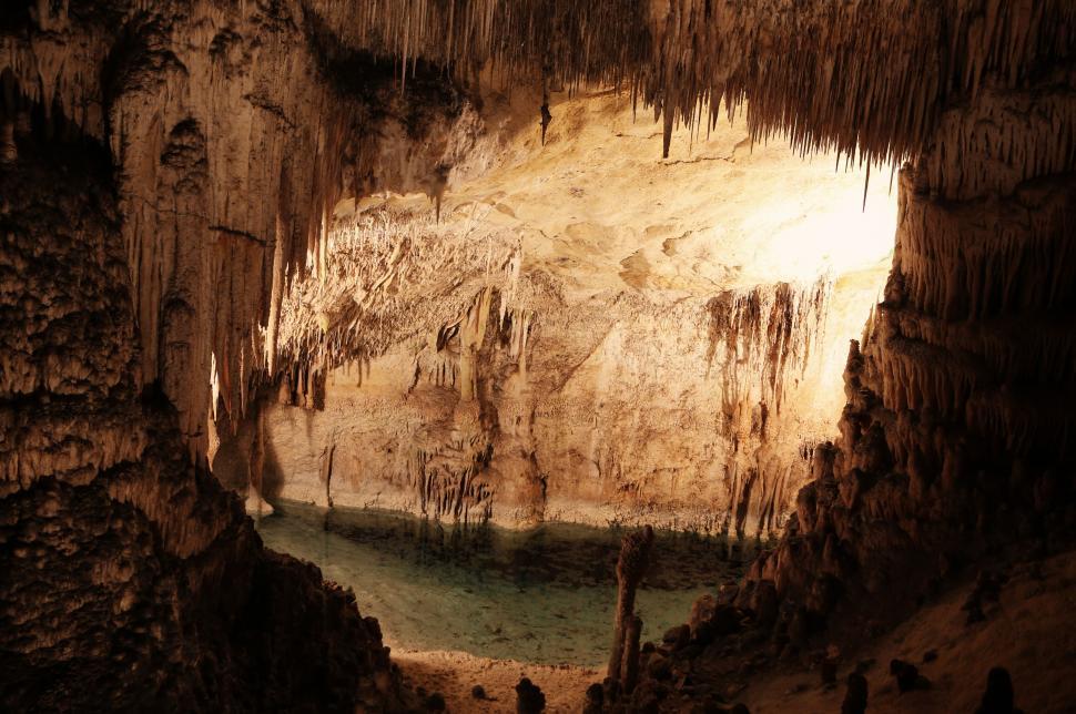 Free Image of Vast cave with a serene underground pool illuminated by soft light 