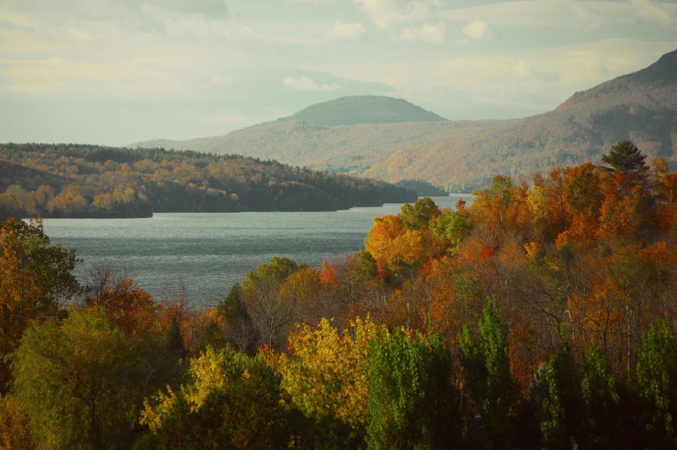 Free Image of Panoramic view of a tranquil lake surrounded by autumnal foliage and hills 