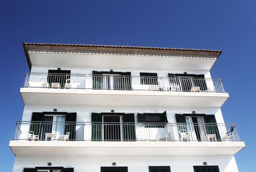 Free Image of Three-story white building with balconies on a clear blue sky day. 