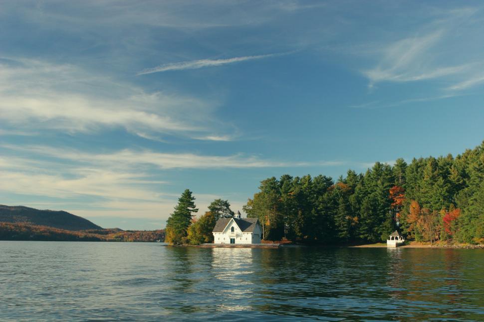 Free Image of Scenic lakeside house surrounded by trees, reflecting on calm water. 