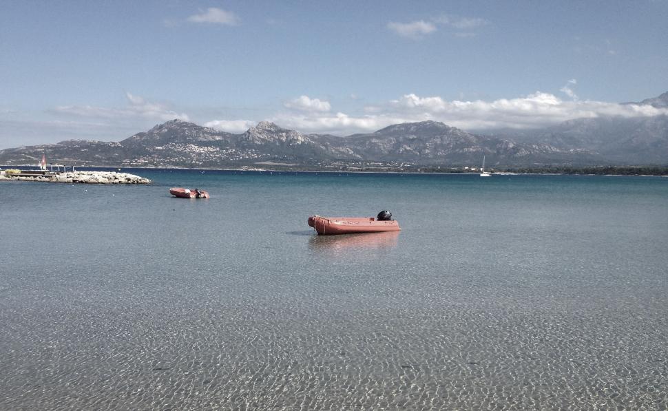 Free Image of Tranquil lake with boats and mountains in background under clear sky. 