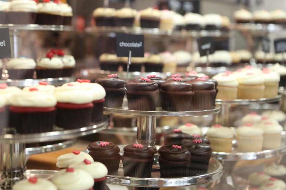 Free Image of Variety of cupcakes displayed on tiered stands in a bakery shop. 