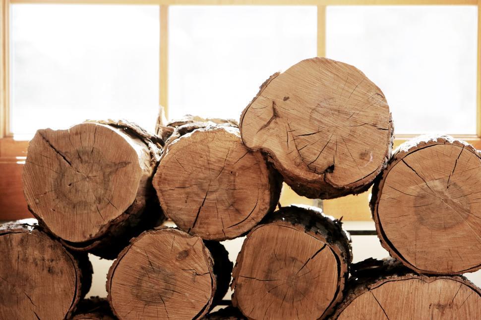 Free Image of Stacked tree logs indoors near bright window in warm light 