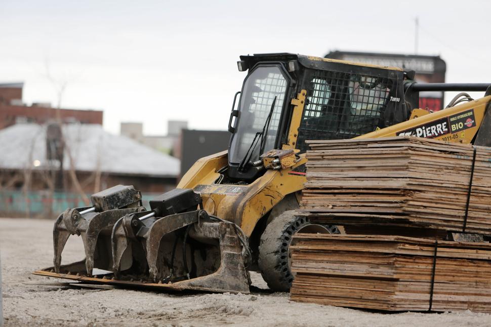 Free Image of Front view of a yellow loader lifting wooden planks on construction site 