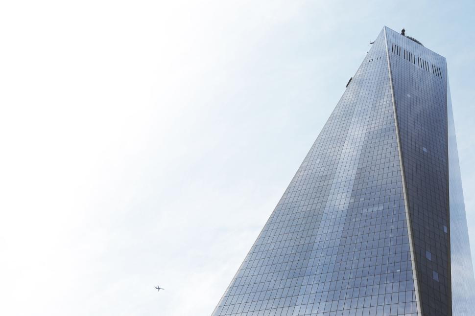 Free Image of Modern glass skyscraper towering into the sky with an airplane 