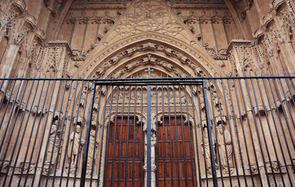 Free Image of Facade of an ancient cathedral with elaborate carvings and iron gate 
