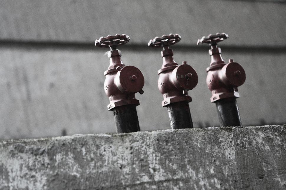Free Image of Three red industrial valves on a concrete wall, pipeline control system. 