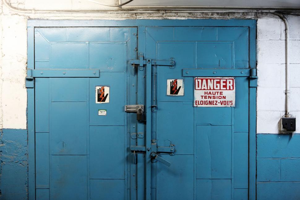 Free Image of Blue industrial doors with high voltage danger warning signs  visible. 