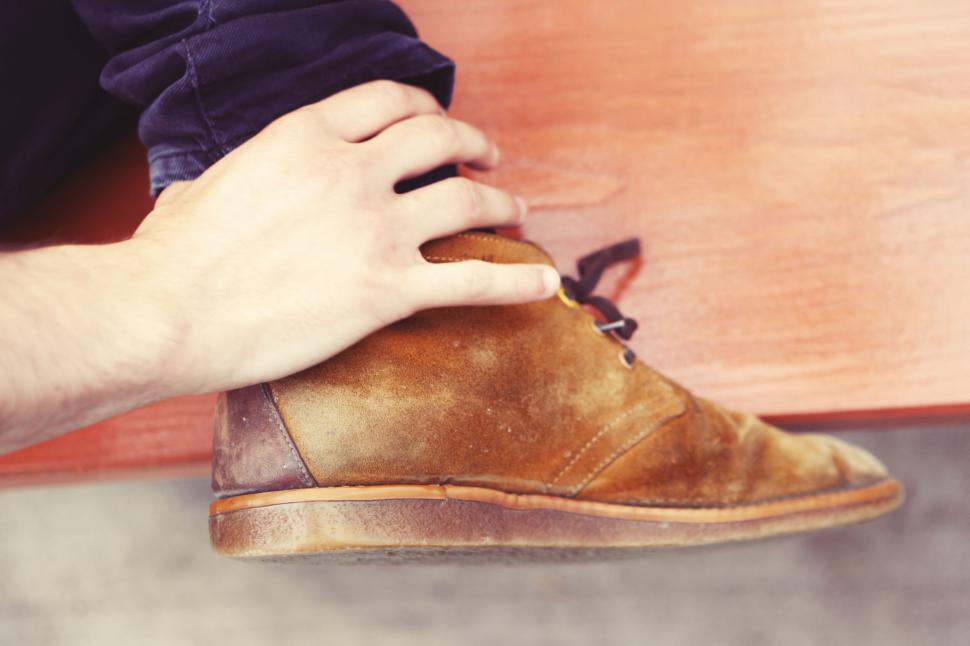 Free Image of Brown leather shoe being tied by a person sitting on a bench 