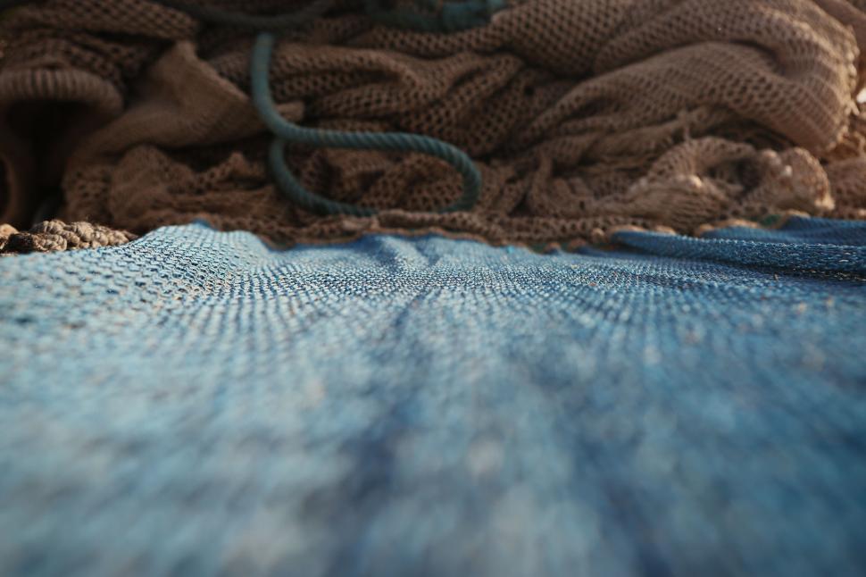 Free Image of Close-up shot of blue fishing net with brown nets piled behind it. 