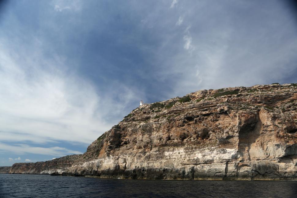 Free Image of Coastal cliffside with lighthouse and dramatic cloudy sky above 