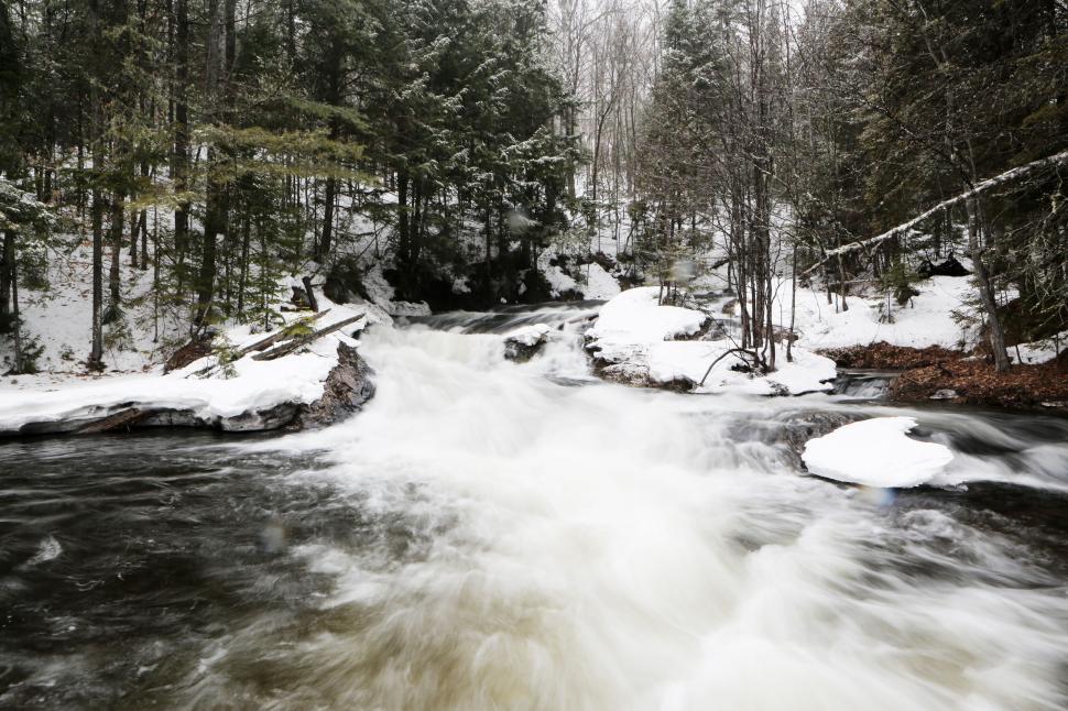 Free Image of A tranquil snow-covered forest with a rushing river in winter. 