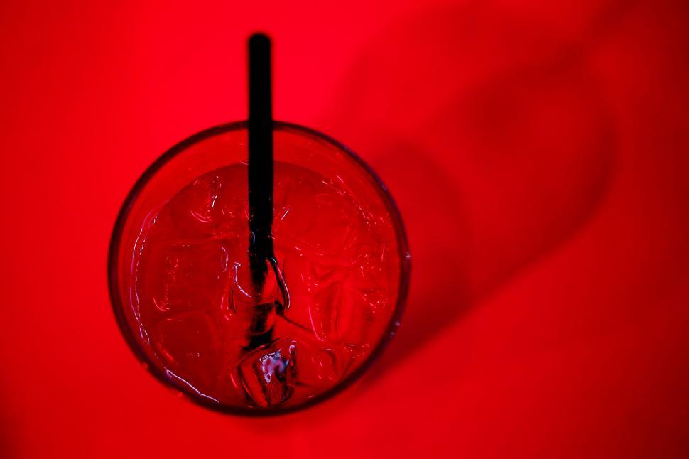 Free Image of Top view of a red cocktail with ice and black straw on red background 