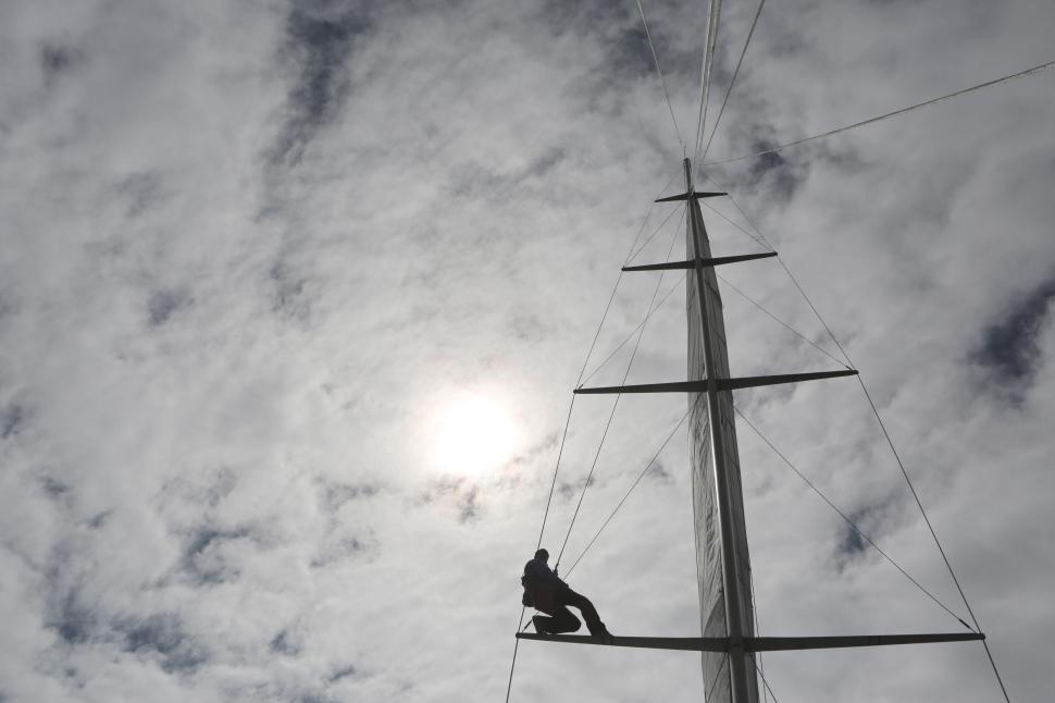 Free Image of Person climbs sailboat mast against dramatic cloudy sky backdrop 