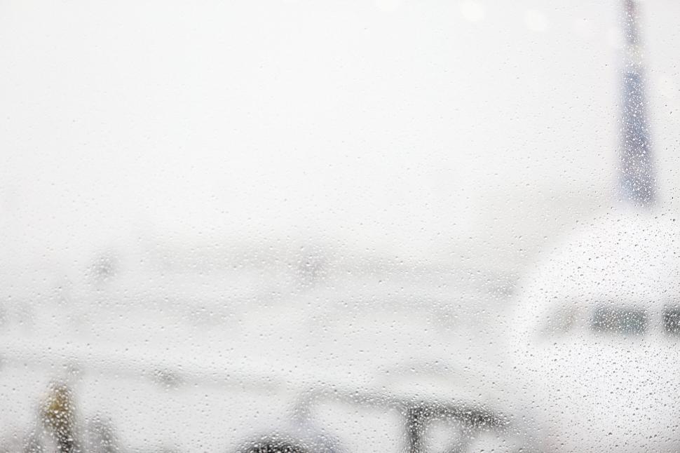 Free Image of Blurry airplane and airport viewed through raindrop-covered window. 