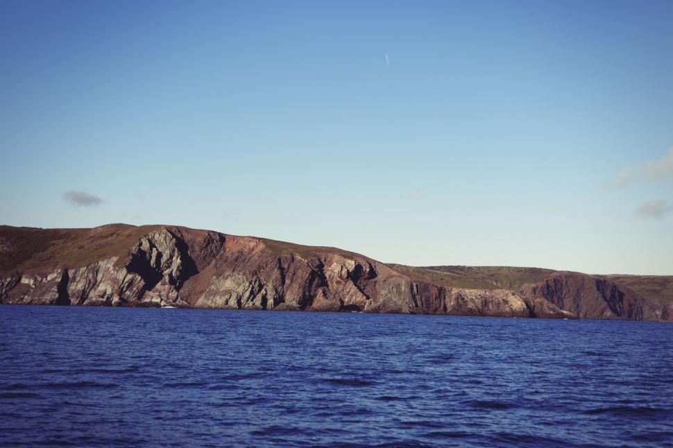Free Image of Rocky coastal cliffs overlooking a calm blue ocean and clear sky. 