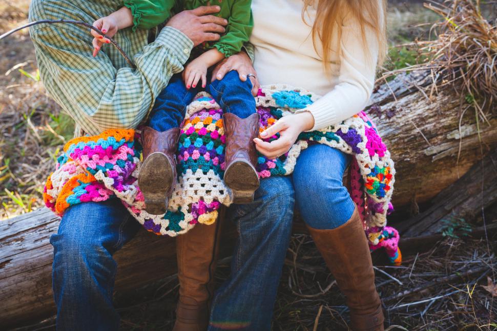 Free Image of Family sitting on a log with colorful crocheted blanket around them. 