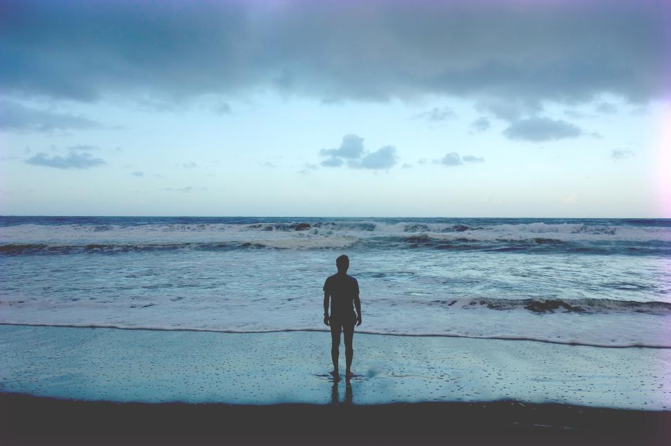 Free Image of Silhouette of person standing on the shore facing the vast ocean 