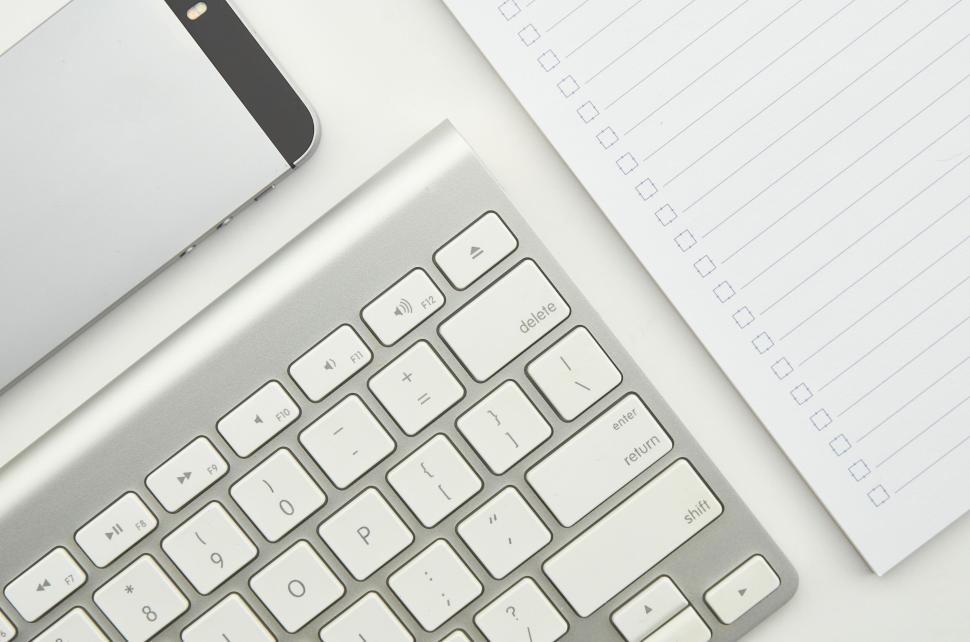 Free Image of White wireless keyboard and blank notepad on a white desk surface 