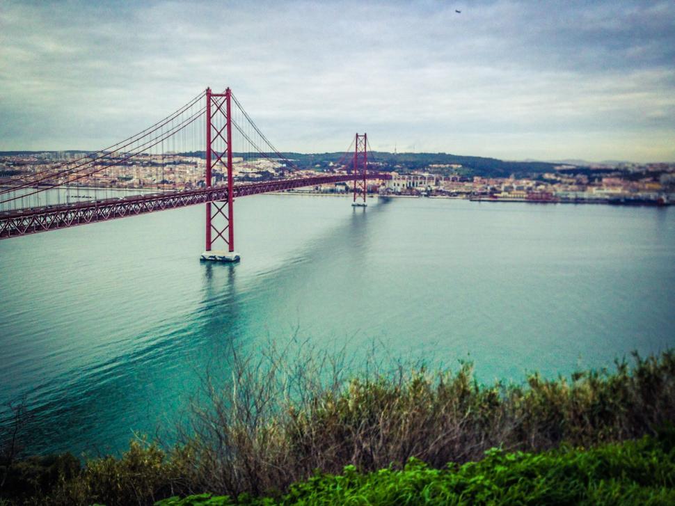 Free Image of Red bridge stretching across a serene body of water in the city 