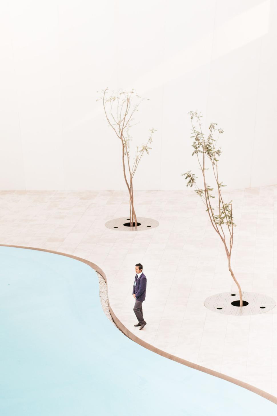 Free Image of Man walking next to a minimalist pool with two barren trees near 