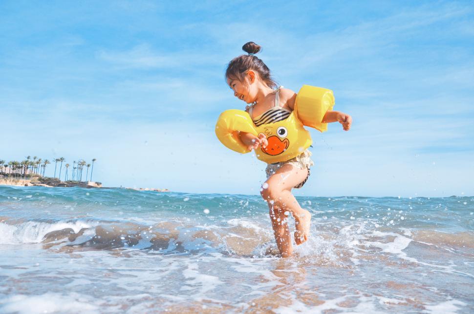 Free Image of Child enjoying the beach with inflatable armbands on sunny day. 