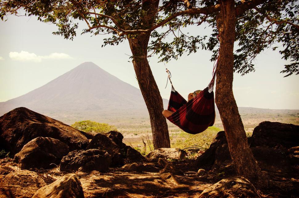 Free Image of Person relaxes in hammock under two trees with mountain in background 
