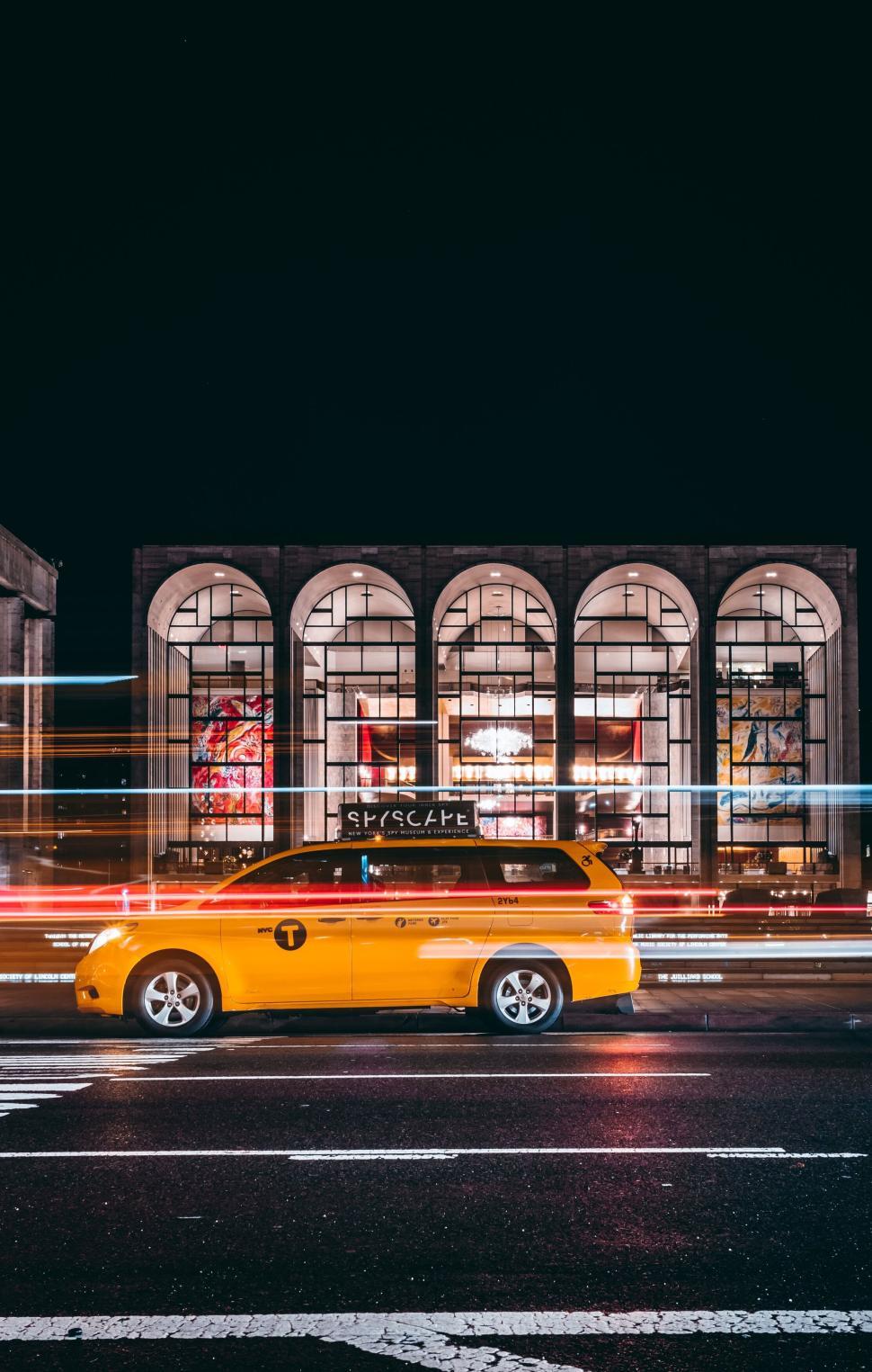 Free Image of Yellow taxi driving at night with colorful city lights background 