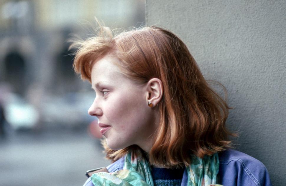Free Image of Woman with red hair wearing a scarf standing against a wall 