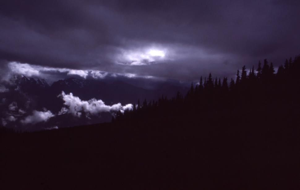 Free Image of Storm clouds over a darkened mountain landscape at dusk 