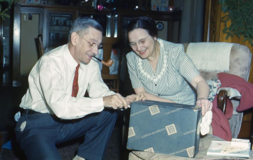 Free Image of Elderly couple unwrapping present, man smoking a pipe indoors. 