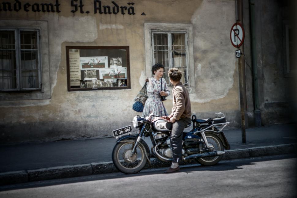 Free Image of Vintage scene with a motorcycle and two people chatting 