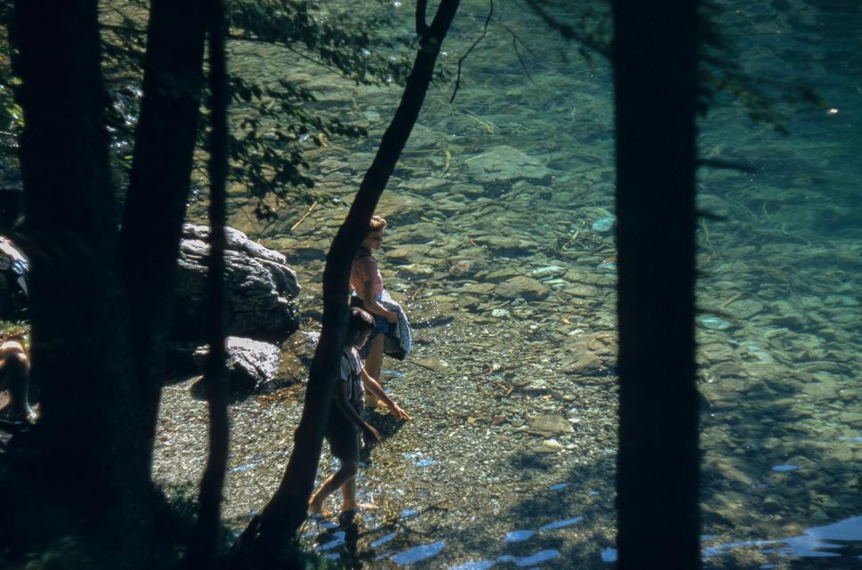 Free Image of Two people enjoy a day by the transparent, rocky lake in the forest. 