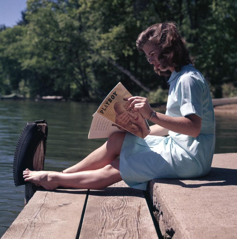 Free Image of Woman reading on dock by peaceful lake, enjoying leisure time 