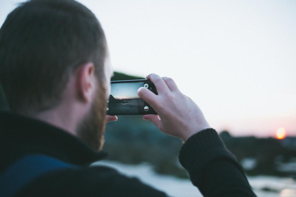 Free Image of Person capturing a sunset beach view with a smartphone camera. 