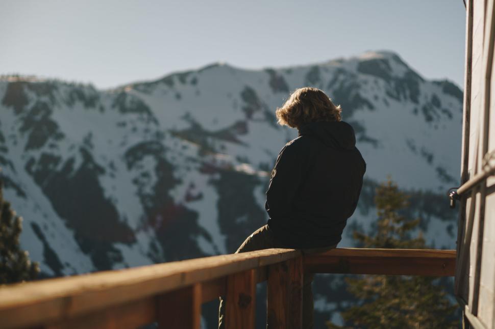 Free Image of Person sitting on wooden railing with snowy mountain background. 