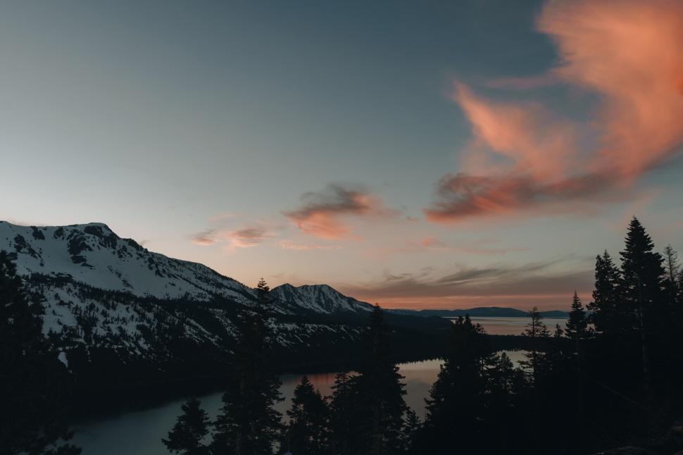 Free Image of Snowy mountain range and lake at sunset with trees in foreground. 